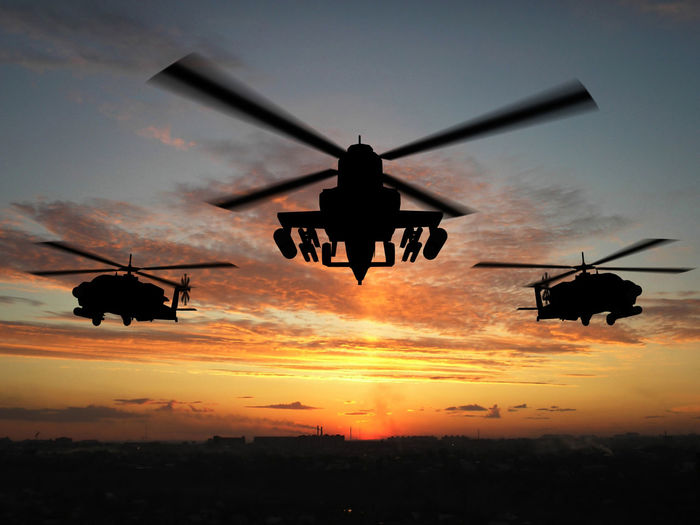 Military helicopters flying over cityscape against sky during sunset