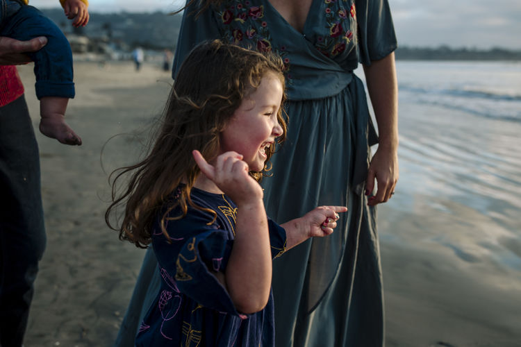 Laughing 3 yr old girl in dress at beach with family