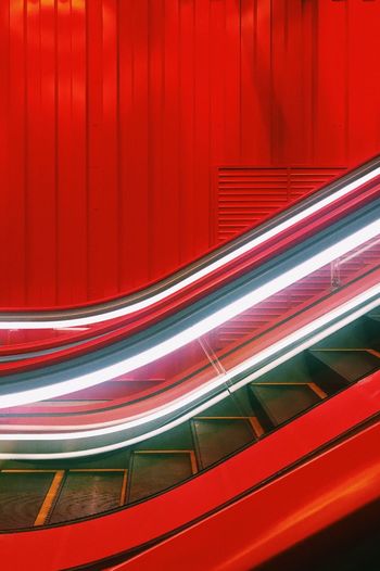 Close-up of illuminated escalator by red wall