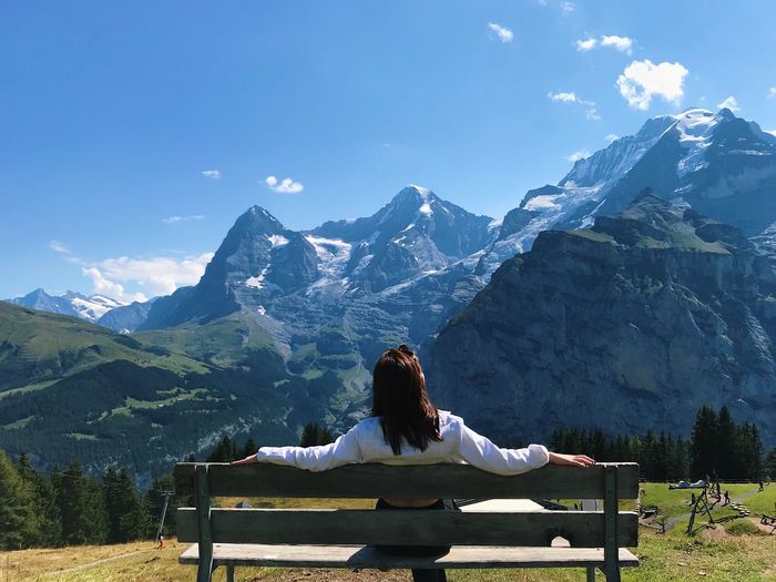 Rear view of woman sitting on bench against mountain range