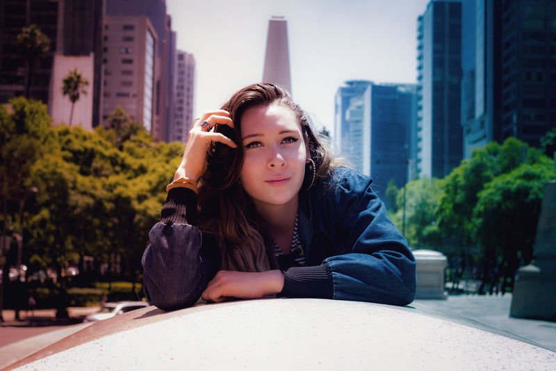Portrait of young woman sitting against buildings in city