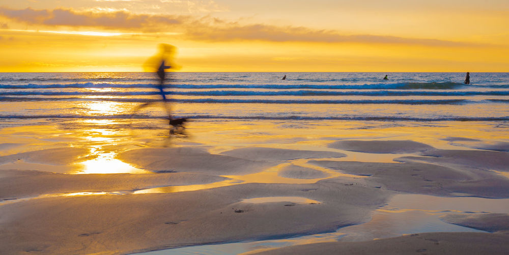 Blurred person running on shore at beach against orange sky during sunset