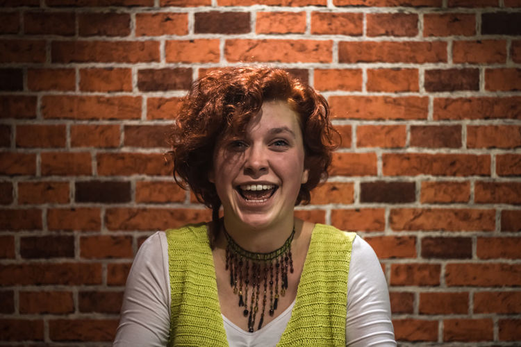 Portrait of happy young woman against brick wall