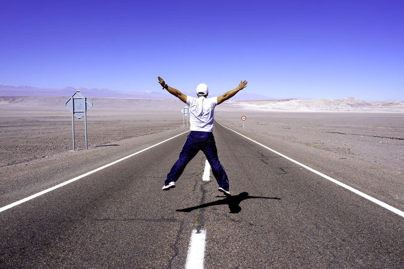 Man with arms raised on road against sky