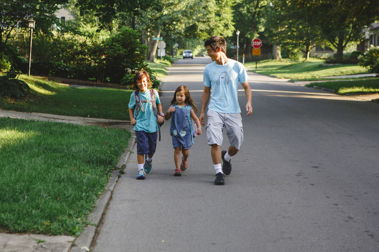 Full length of father and children walking on road to school