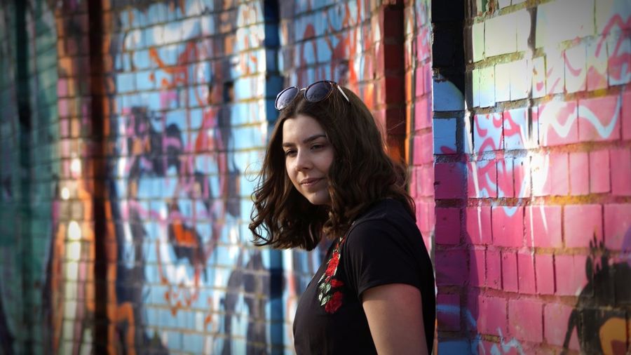 Thoughtful woman standing against colorful graffiti wall