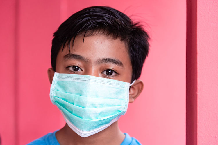 Portrait of a teenager with a face mask, pink background
