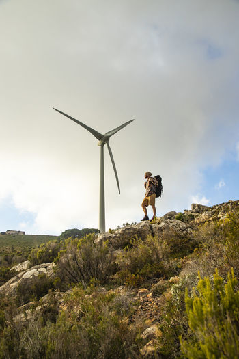 Spain, andalusia, tarifa, man on a hiking trip standing on rock with wind turbine in background