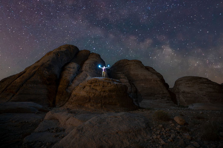 A man holding light at night on a rock canyon facing the milky way