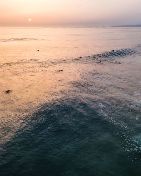 Aerial view of people waiting for waves to surf at sunset in atlantic ocean open water