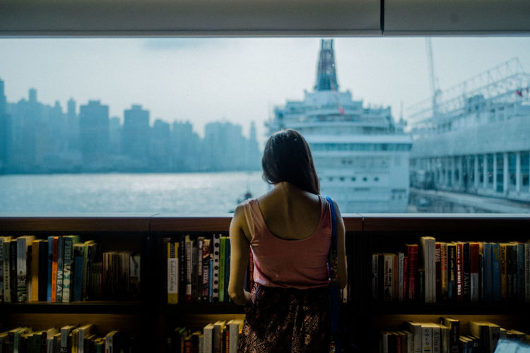 Rear view of woman standing in library against sky