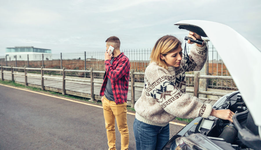 Woman repairing car while man talking on phone