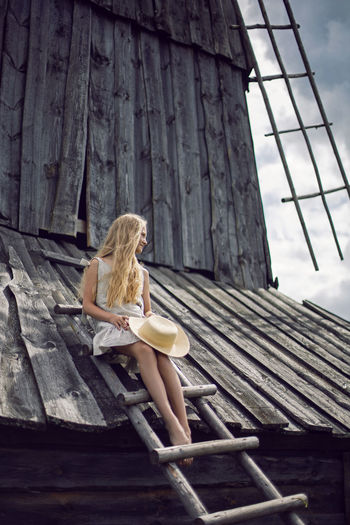 Low angle view of woman sitting on wooden wall
