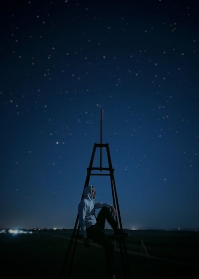 Silhouette man sitting on field against sky at night