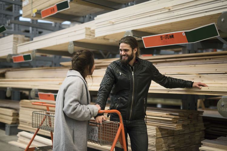 Smiling man standing with woman by wooden planks on shelves at hardware store