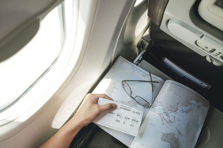 Cropped hand of man holding map and ticket in airplane