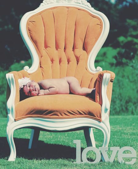 Naked baby girl sleeping on chair by love text at field
