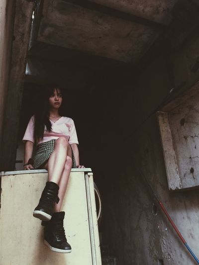 Low angle view of woman sitting on abandoned refrigerator