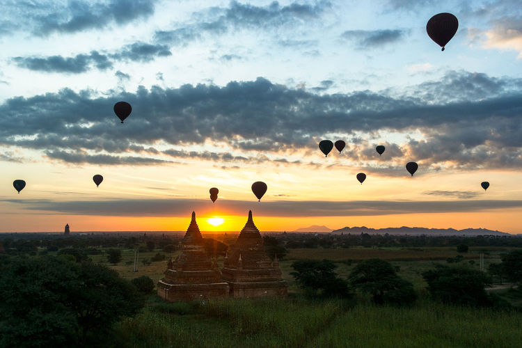 Hot air balloons flying over temples against sky during sunrise