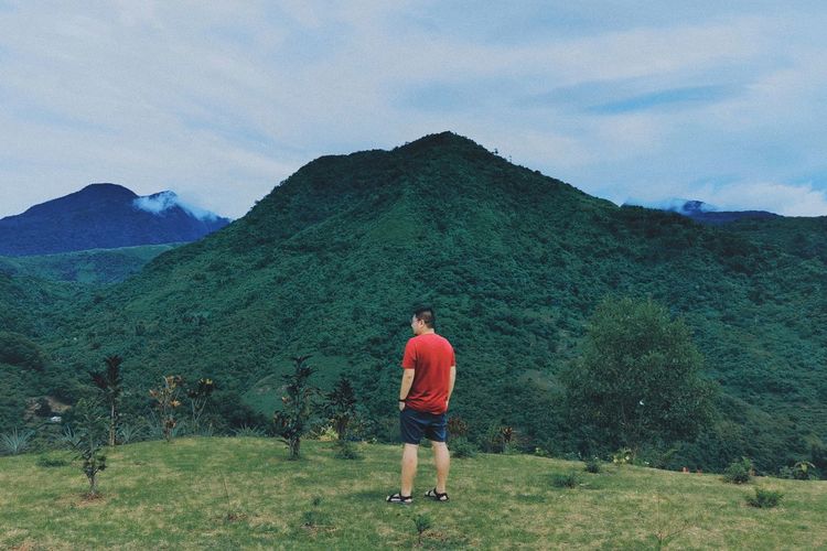 Rear view of man standing on mountain against sky