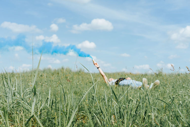 Woman holding smoke bomb while lying down on field
