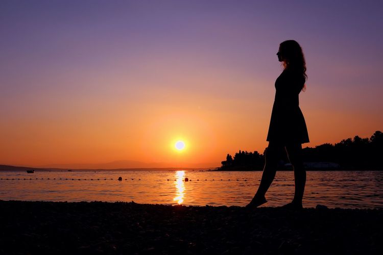 Silhouette woman walking at beach against sky during sunset