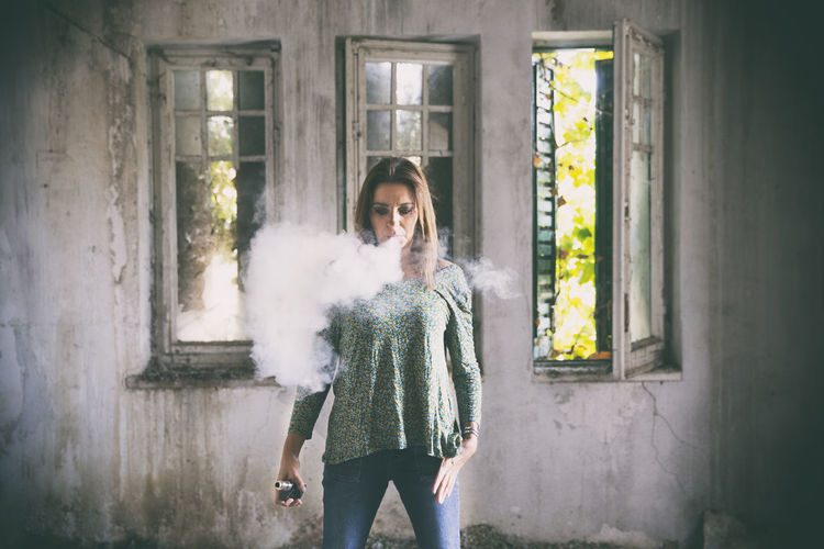 Woman exhaling smoke against wall