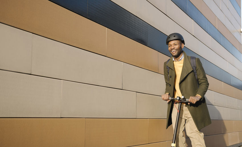 Happy man with helmet and scooter passing a building