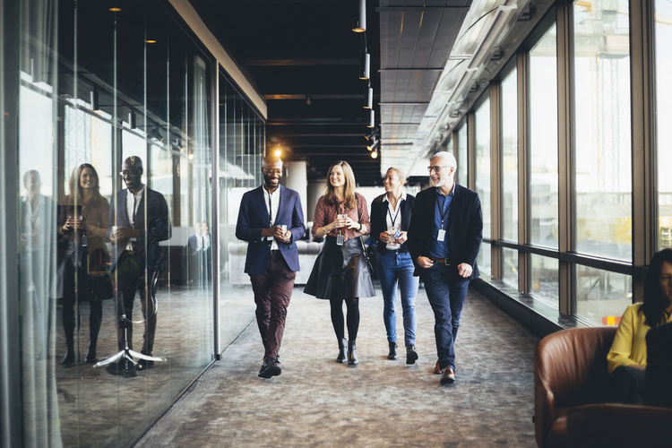 Smiling female and male colleagues walking in corridor at workplace