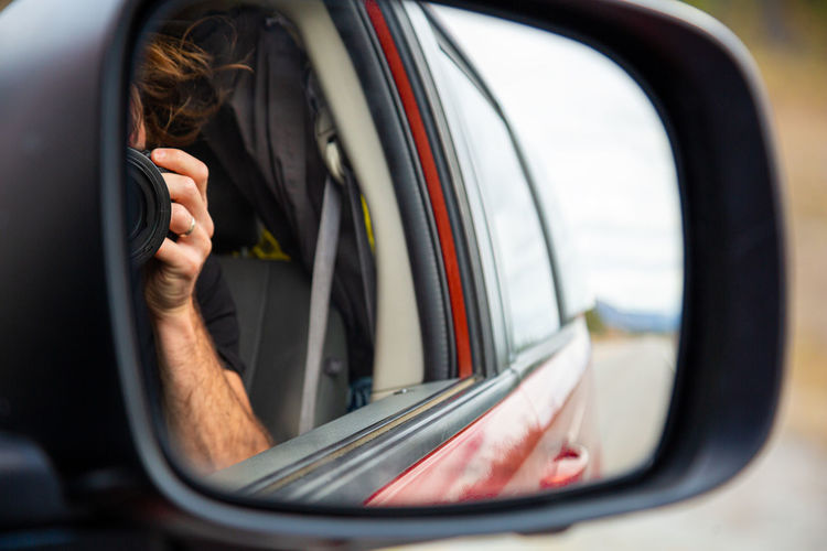 Man photographing with camera reflecting on side-view mirror