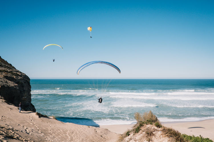 People paragliding over sea against clear blue sky