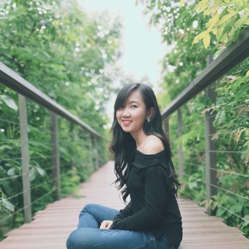 Portrait of smiling young woman sitting on footbridge