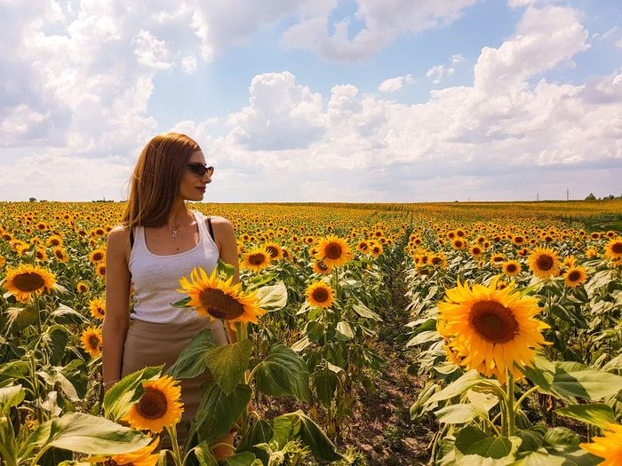 Girl standing with in a sunflower  field against cloudy sky