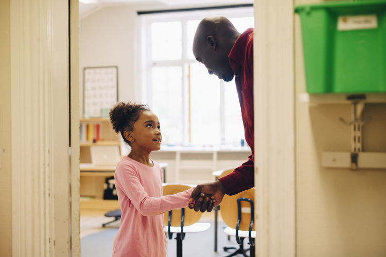 Teacher shaking hand with boy at doorway in classroom