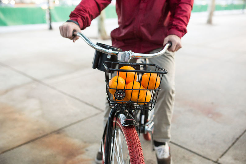 Midsection of man cycling with fresh oranges in basket