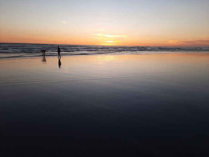 Lover couple walking on wet sand beach at sunset