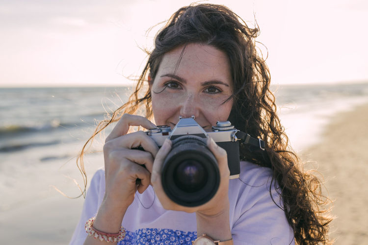 Young woman photographing with camera while standing at beach
