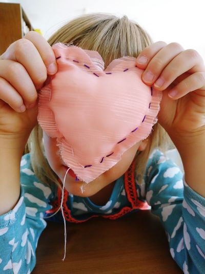 Close-up of girl covering face with heart shape at home