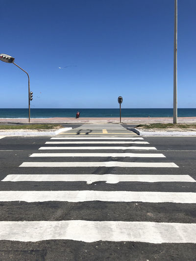 Zebra crossing on road by sea against clear sky