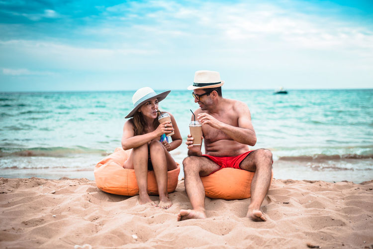 Mature couple having drinks while sitting at beach