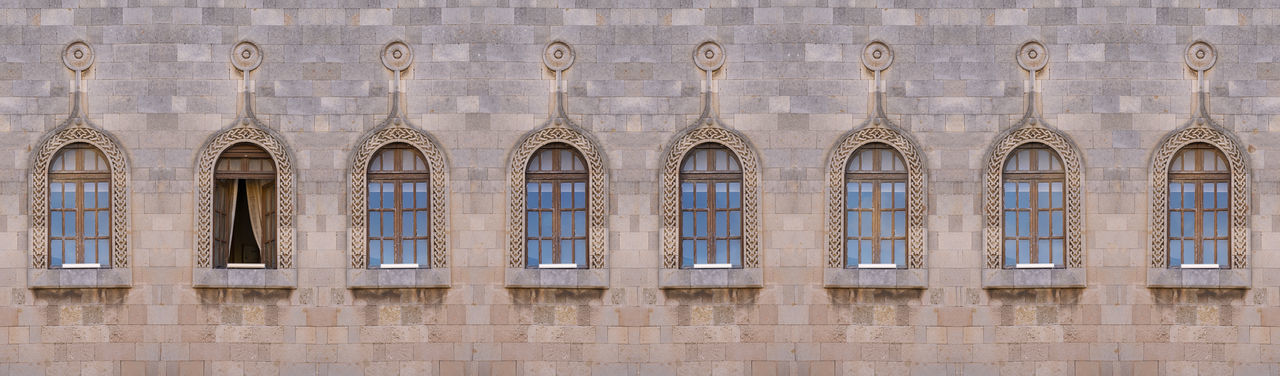 Wooden antique arch windows in a row all closed only one is open.