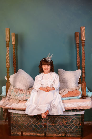 A beautiful little princess is sitting on a vintage wooden bed