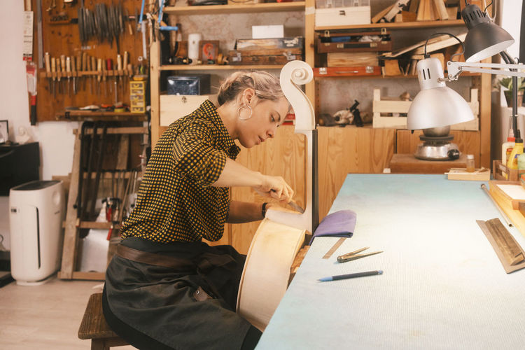 Luthier with hand tool carving on double bass at workshop