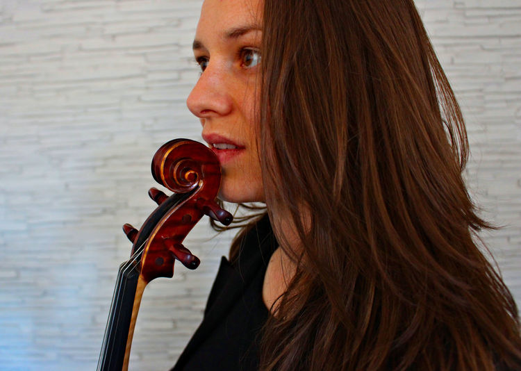 Close-up of woman holding violin against wall