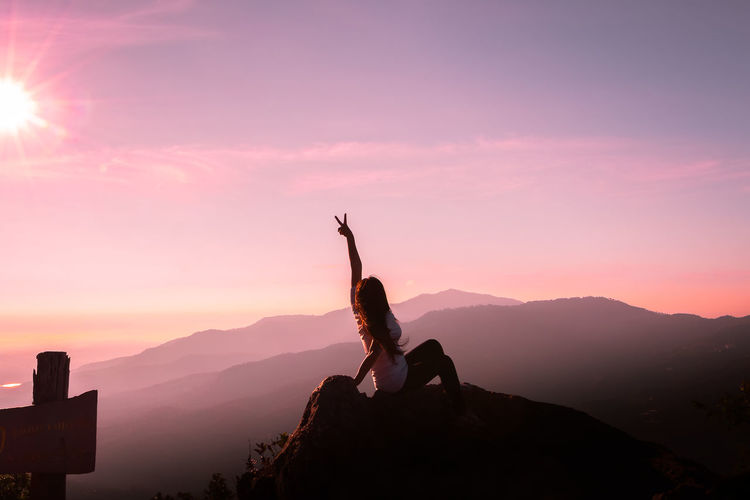 Woman climbing on mountain against sky during sunset