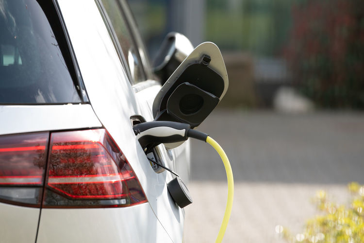 Plug in adapter in car charge battery of electric car next to a charging station with yellow cable