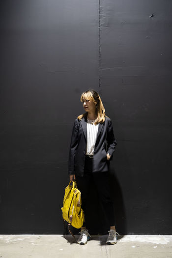 Businesswoman with backpack standing against wall at railroad station