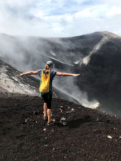 Rear view of woman standing with arms outstretched at volcanic crater
