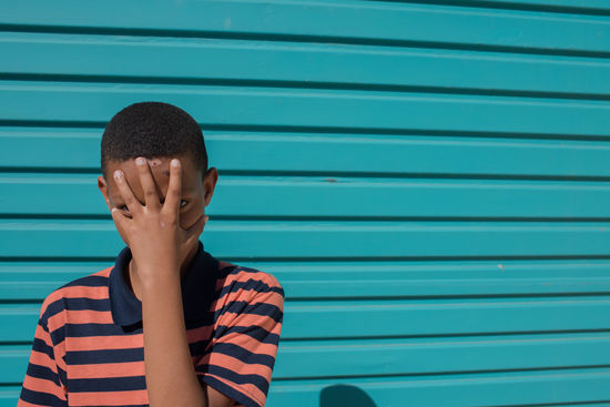 Portrait of boy covering face with hand against shutter