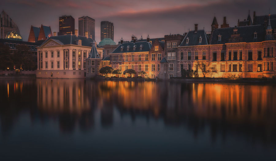 Reflection of buildings in river against sky during sunset